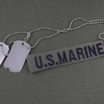 Military dog tags and a U.S. Marines name tape on a green background