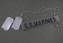 Military dog tags and a U.S. Marines name tape on a green background