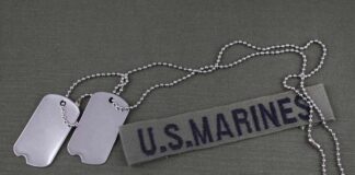 Military dog tags and a U.S. Marines name tape on a green background