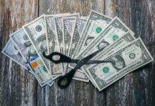 Army Training Slashed As Billions Vanish Scissors placed on a spread of various U.S. dollar bills