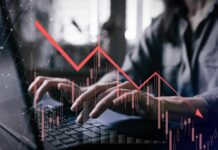 Person typing on a laptop with a declining stock market graph overlay