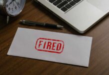 Another 8,000 Jobs Cut — AI’s Costly Reality Check An envelope marked 'FIRED' on a wooden desk next to a clock and a laptop