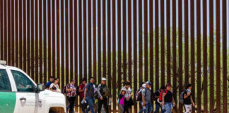Group of people walking by a border fence.