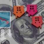 Colorful house icons on a background of hundred dollar bills with a downward trend graph