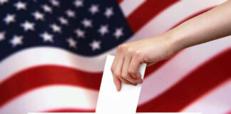 Hand dropping ballot into box, American flag background.