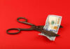 Funding Axe Hangs Over States Due To THIS! Scissors cutting a hundred dollar bill on a red background