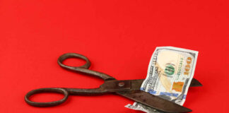 Scissors cutting a hundred dollar bill on a red background