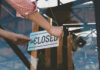 175 Store Closures Announced Person flipping closed sign on glass door