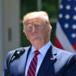 Shock Trump Pick Stuns Leftists Donald Trump speaking with US flag in the back.