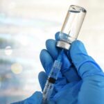 A gloved hand holding a syringe and a vial of liquid