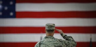 A military personnel saluting in front of a large American flag