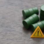 Four green barrels and a warning sign on a wooden surface