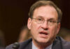 Justice Alito Drops Border Bomb Samuel Alito speaking into a microphone.