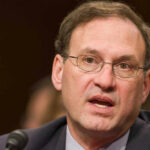 Justice Alito Drops Border Bomb Samuel Alito speaking into a microphone.