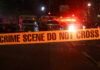Crime scene tape with emergency vehicles in background.