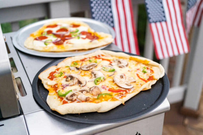 Homemade pizzas on grill trays with vegetable and pepperoni toppings