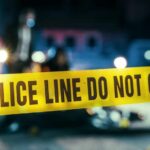 Grim Stench Leads To School Horror Police line caution tape at a crime scene with blurred figures in the background