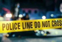 Grim Stench Leads To School Horror Police line caution tape at a crime scene with blurred figures in the background