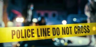 Police line caution tape at a crime scene with blurred figures in the background