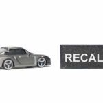 Seats Flip Mid-Drive — Big Recall A miniature gray sports car next to a black sign that reads 'RECALL'