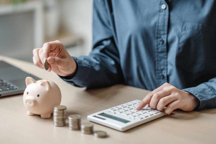 Person placing a coin into a piggy bank while using a calculator