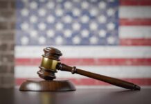 A wooden gavel resting on a sound block with an American flag background