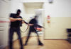 Grocery Store Gunfight: Shots Erupt Mid‑Aisle Two masked individuals with guns moving quickly in a hallway