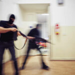 Grocery Store Gunfight: Shots Erupt Mid‑Aisle Two masked individuals with guns moving quickly in a hallway