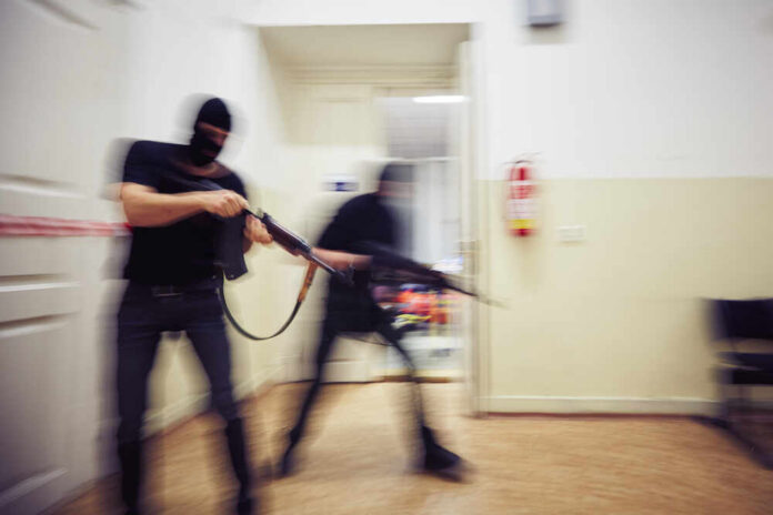 Two,Terrorists,With,Rifles,In,The,Building,-,De,Focused Two masked individuals with guns moving quickly in a hallway