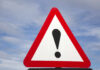 Warning road sign with exclamation mark against a cloudy sky