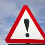 Warning road sign with exclamation mark against a cloudy sky