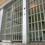 ICE Jail Death Sparks Fury Empty prison cell with metal bars and toilet.