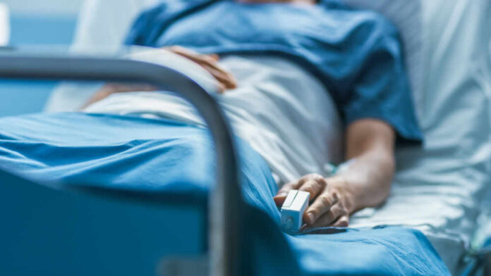 In,The,Hospital,Sick,Male,Patient,Sleeps,On,The,Bed. A patient lying in a hospital bed with a monitoring device in hand