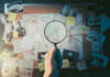 Magnifying glass over investigation board with photos and strings.