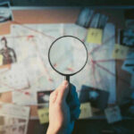 Magnifying glass over investigation board with photos and strings.