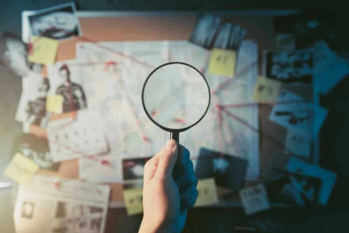 shutterstock_1192132651-1 Magnifying glass over investigation board with photos and strings.