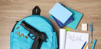 A blue backpack with a handgun and school supplies on a wooden surface