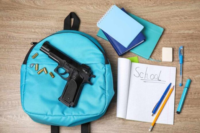 A blue backpack with a handgun and school supplies on a wooden surface