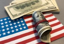 Free Money Frenzy Erupts Nationwide A roll of hundred dollar bills placed on an American flag