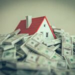 A small model house surrounded by stacks of money