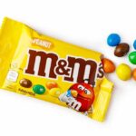 Candy Shake-Up: What’s Missing From M&M’s? M&M's candy bags with scattered colorful candies on a white table