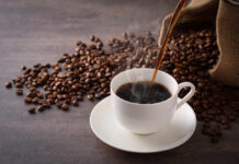 Cup of hot coffee being poured beside scattered coffee beans