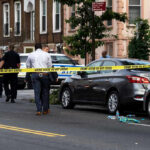 Deadly Drive-By Mass Shooting Shocks Community Police and crime scene tape on city street.