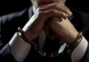 Wild Courthouse Arrest Wrecks Murder Trial Handcuffed person in suit, hands clasped together.