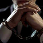 Wild Courthouse Arrest Wrecks Murder Trial Handcuffed person in suit, hands clasped together.