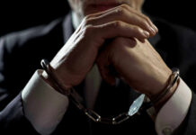 Wild Courthouse Arrest Wrecks Murder Trial Handcuffed person in suit, hands clasped together.