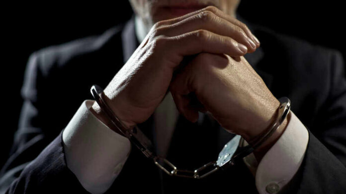 Handcuffed person in suit, hands clasped together.
