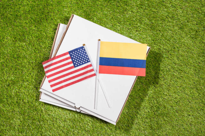 Paper,Box,Of,Pizza,With,Flags,Of,Colombia,And,America USA and Colombia flags on pizza boxes on grass