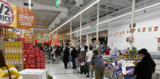 Shoppers queue with carts in a supermarket checkout area