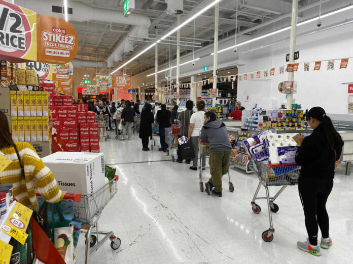 Shoppers queue with carts in a supermarket checkout area